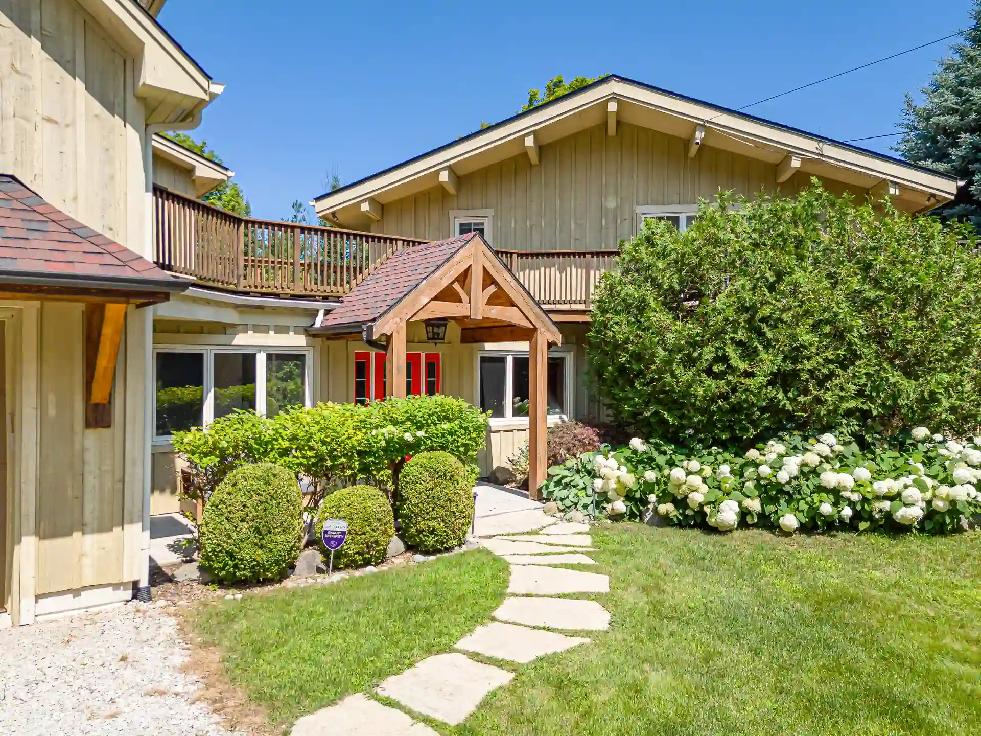 Timber frame cottage entrance with red doors, wraparound deck, and hydrangea garden, worth strong visibility on local and national platforms