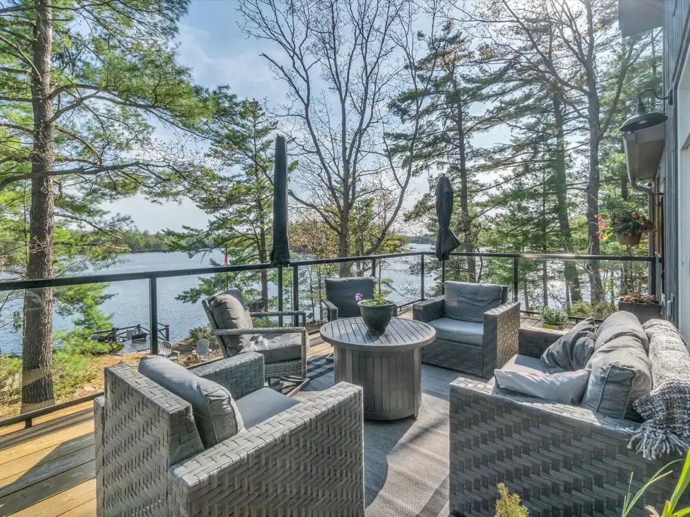 Outdoor lounge deck with modern furniture overlooking a calm Muskoka lake through mature pine trees in Gravenhurst Ontario