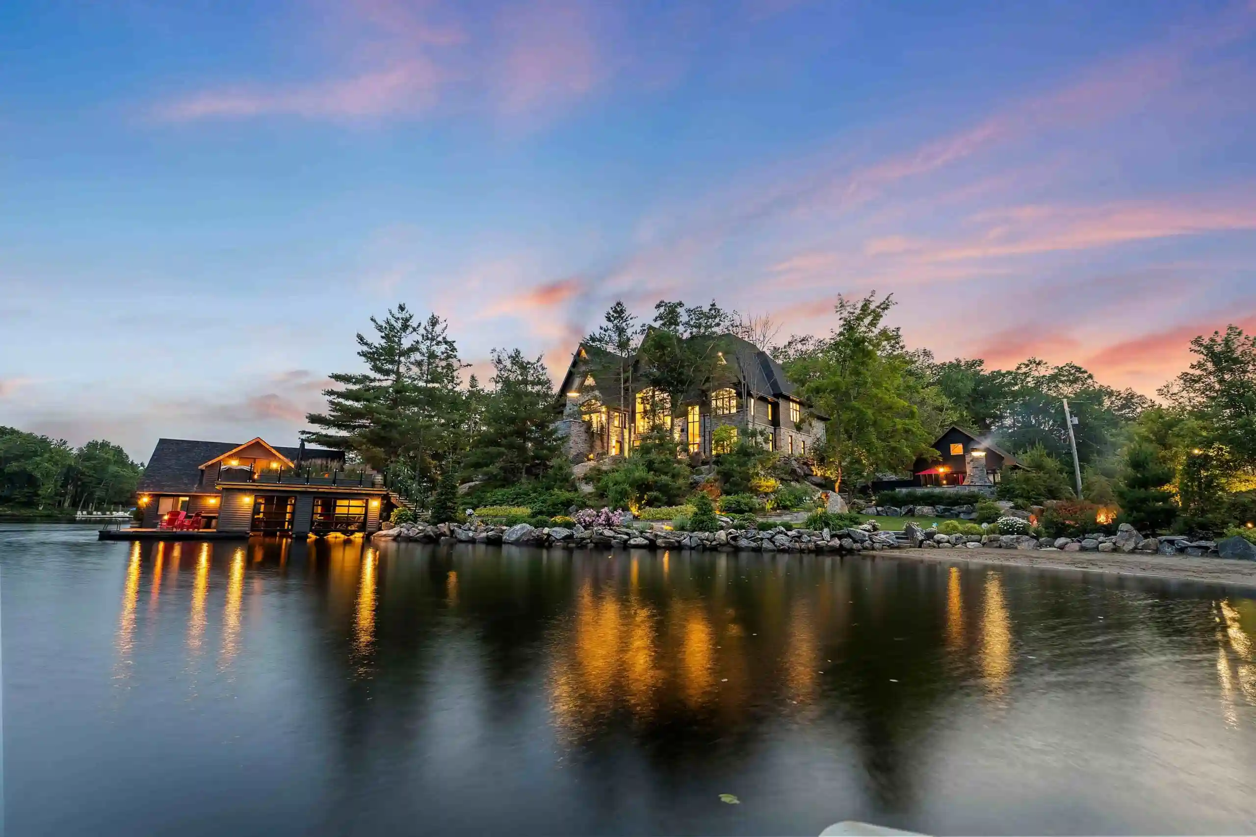 Premium Ontario lakefront cottage with boathouse, stone seawall, and warm lighting reflecting on a calm lake at twilight