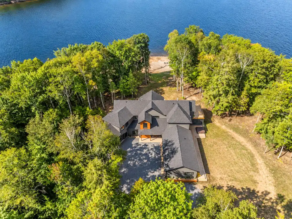 Aerial view of a large Ontario waterfront cottage surrounded by mature trees with a sandy shoreline and direct lake access